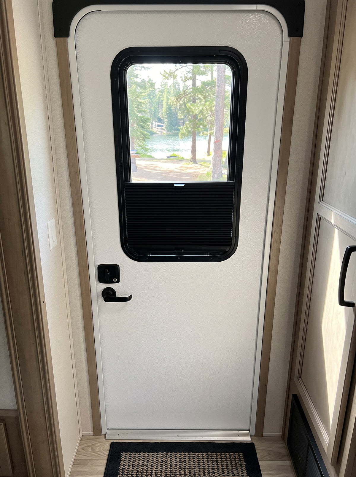 Black cellular RV entry door window shade half open on a 12 x 21 travel trailer door window