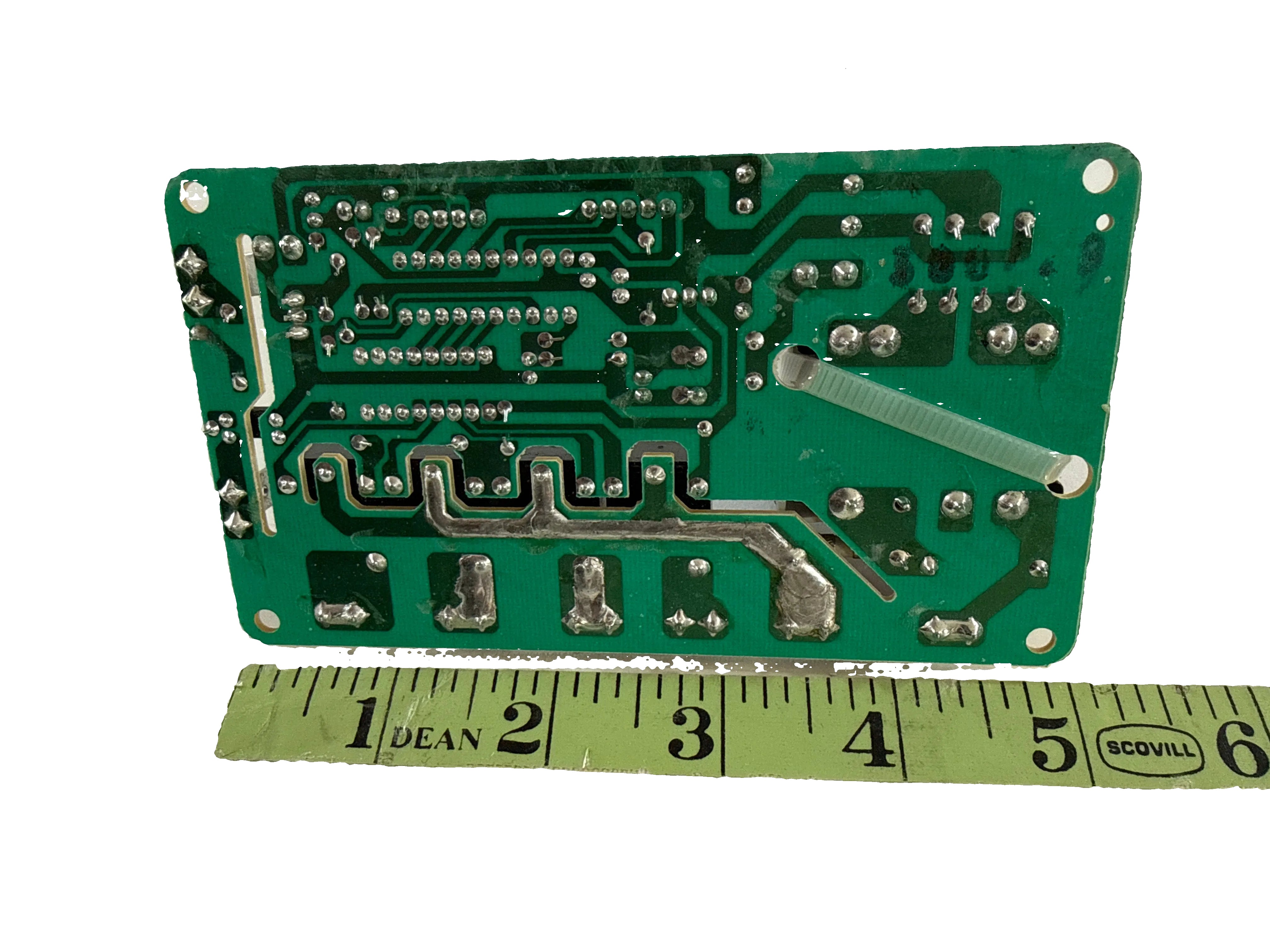 Green circuit board with a ruler for scale on a white background